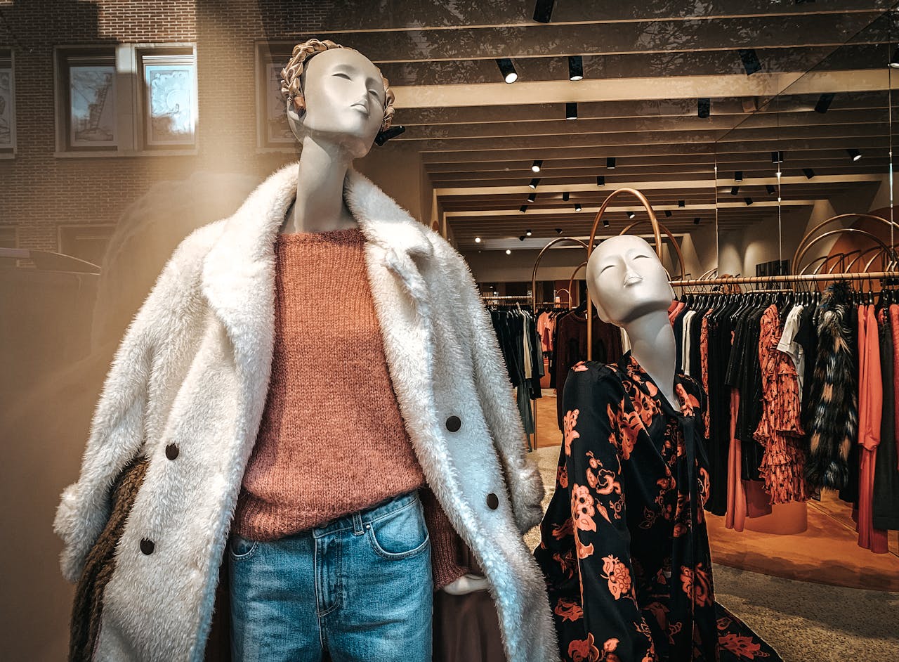 Through glass of clothes shop with mannequins in trendy clothes and stands with dresses